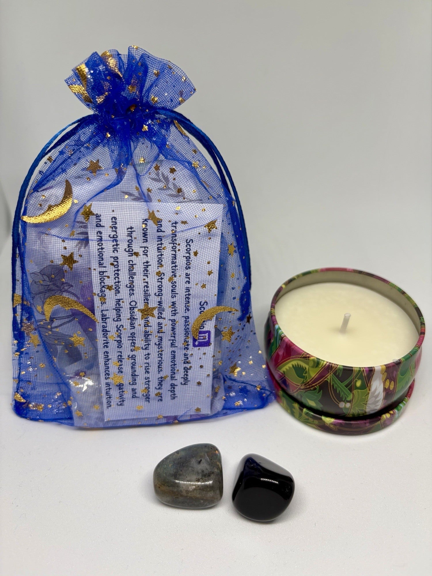 Decorative candle in a tin with a blue gift bag featuring celestial designs on a white background